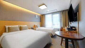 A hotel room with two beds, a desk, a TV, and a window with curtains.