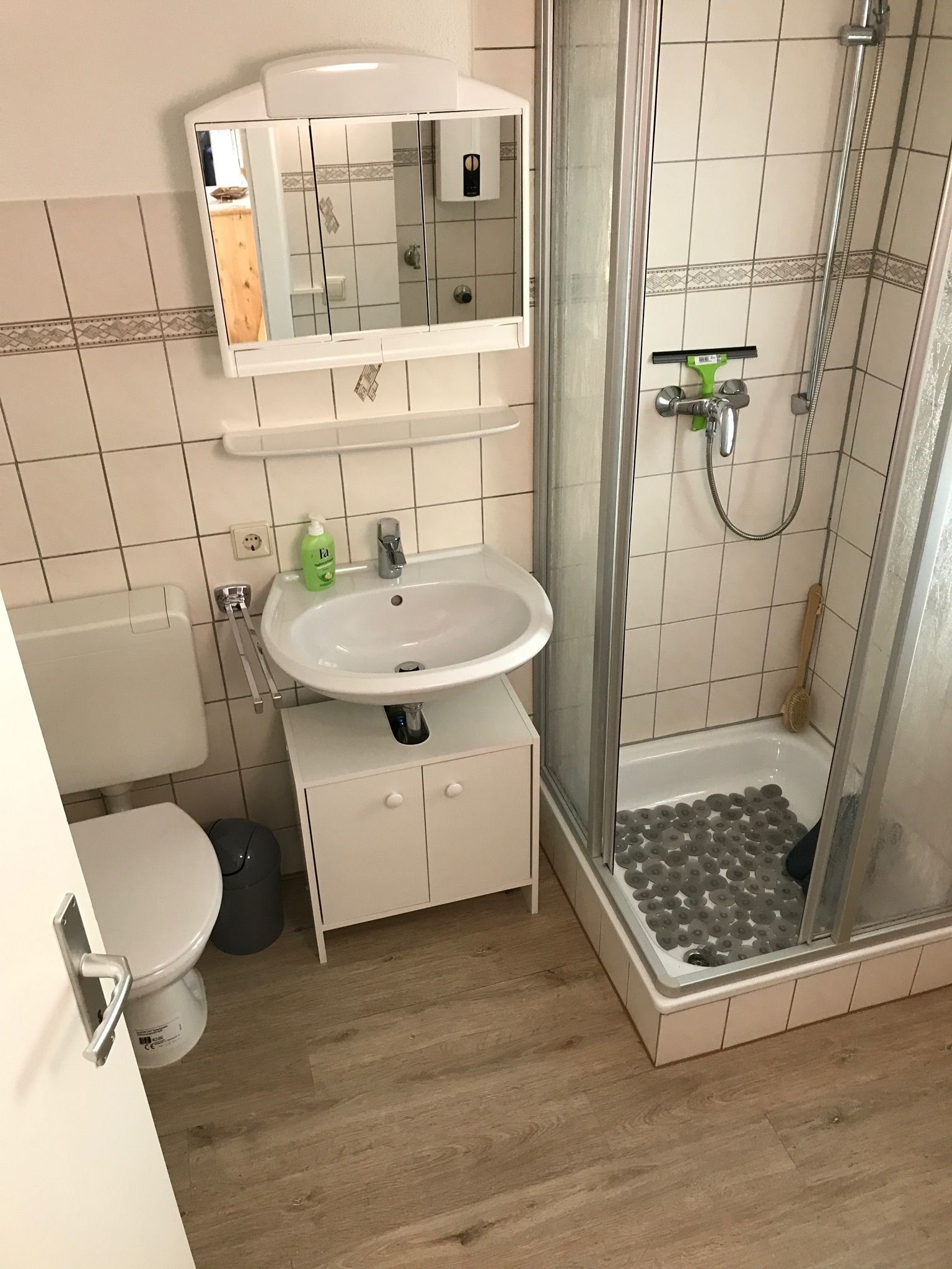Kylpyhuone, jossa on valkoinen pesuallas, peili, lasiovilla varustettu suihku ja wc.