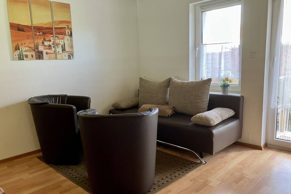 Un salon comprenant un canapé, deux fauteuils, une petite table et une fenêtre donnant sur l’extérieur.