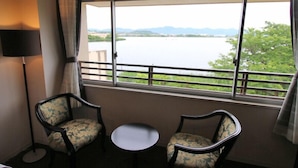 A room with two chairs and a small table, a large window with a view of a body of water and greenery. - Lakeside Hot Spring Hotel Kunibiki (Izumo)