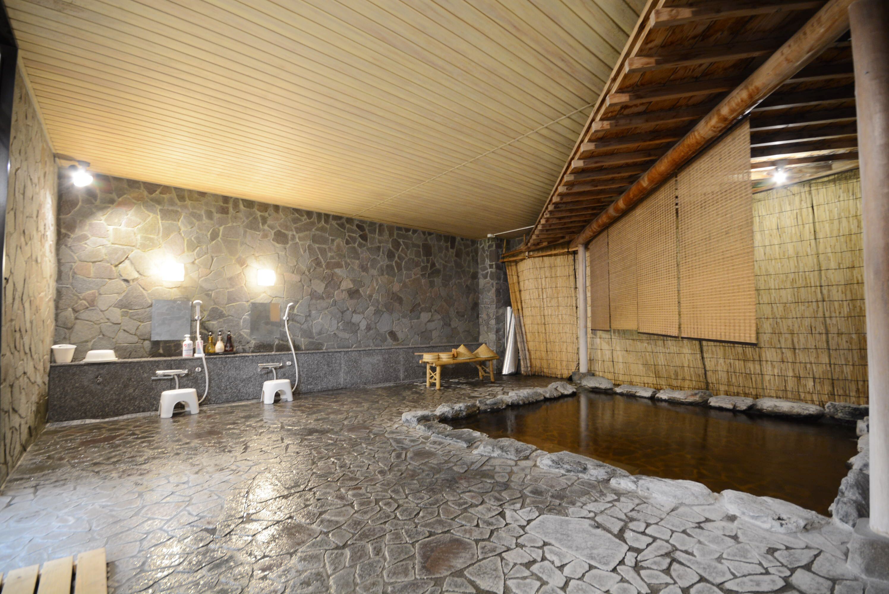 Ein Badezimmer mit Steinsäulen, Holzboden und einem kleinen Holzschemel sowie einem Steingrundbecken.