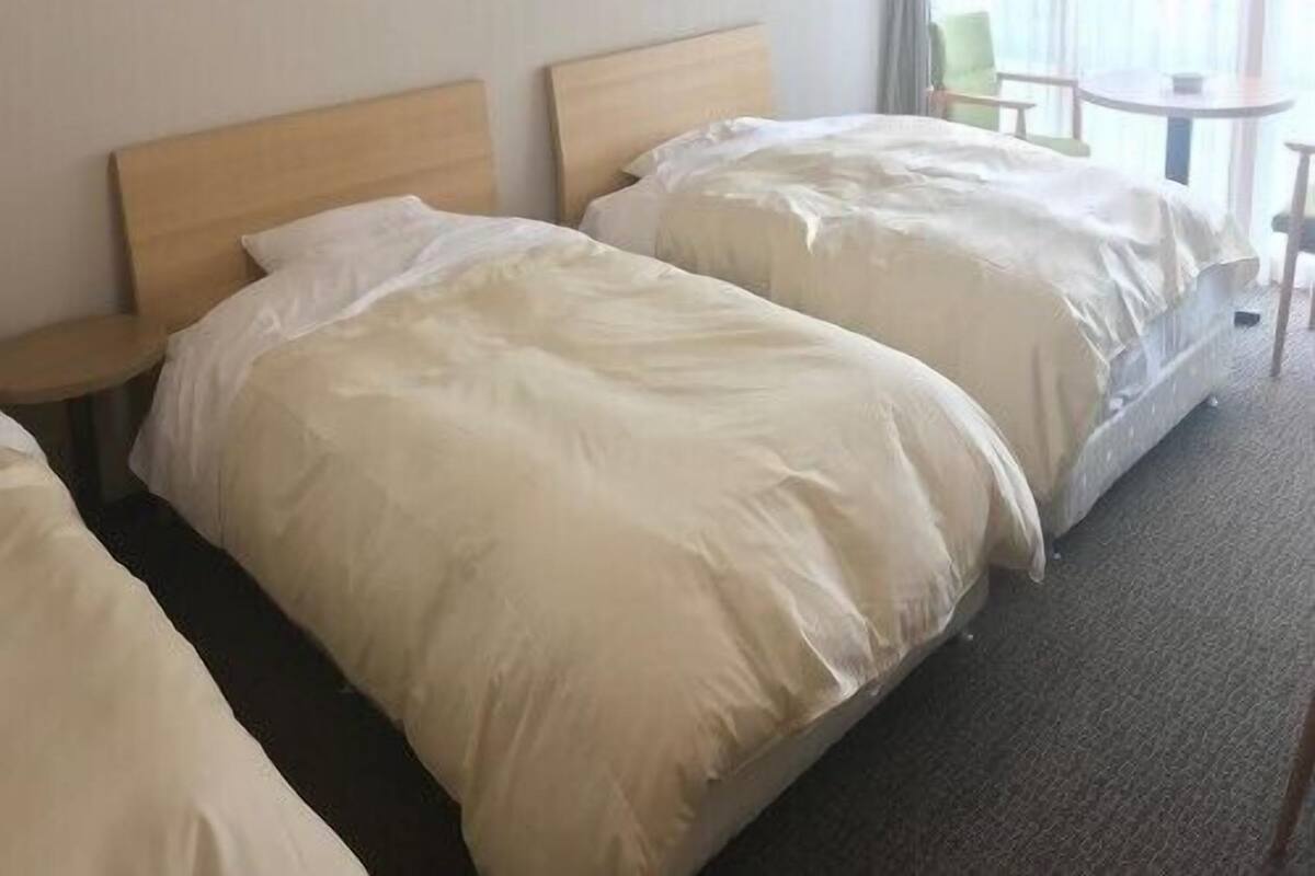 A hotel room with two beds, a small table, and a chair.
