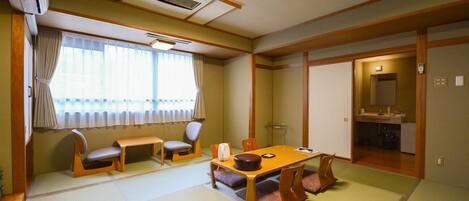 A traditional Japanese room with tatami flooring, a low table with cushions, a sofa, and a sliding door leading to a bathroom.