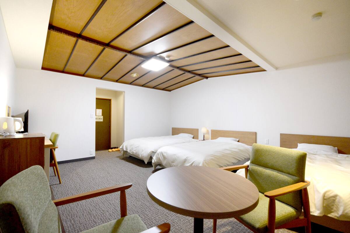 A hotel room with two beds, a desk, a chair, and a round table.