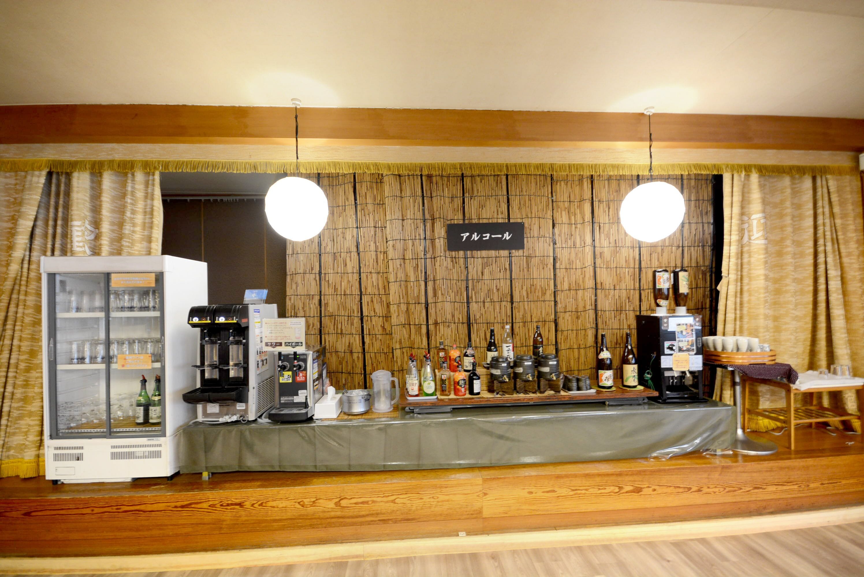 Zona de bar con refrigerador, máquinas de café y una variedad de botellas.