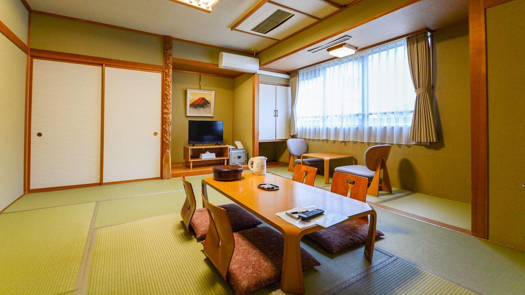 Une pièce de style japonais traditionnel, avec un sol recouvert de tatamis, une petite table basse avec des coussins, un téléviseur et une fenêtre avec des rideaux.