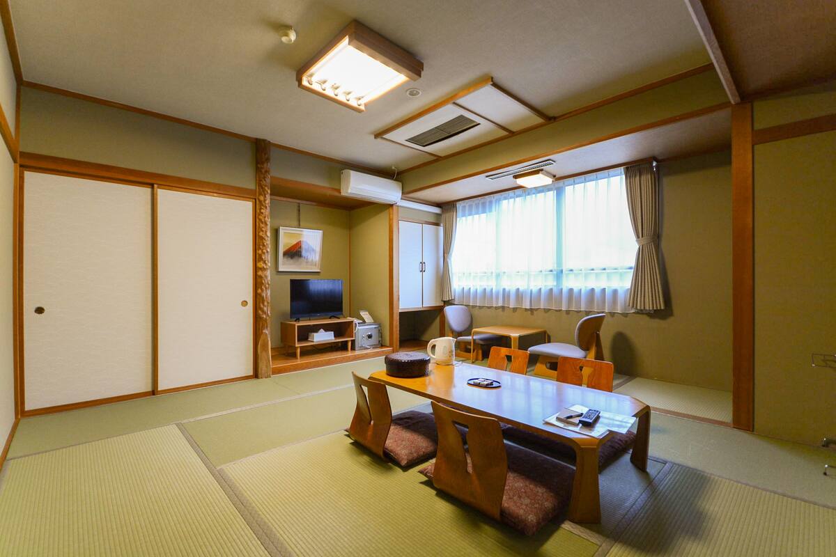 A traditional Japanese-style room with tatami flooring, a low table with cushions, a television, and sliding doors.