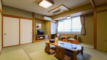 Una habitación tradicional japonesa con suelo de tatami, una mesa baja con cojines, un televisor y puertas correderas.