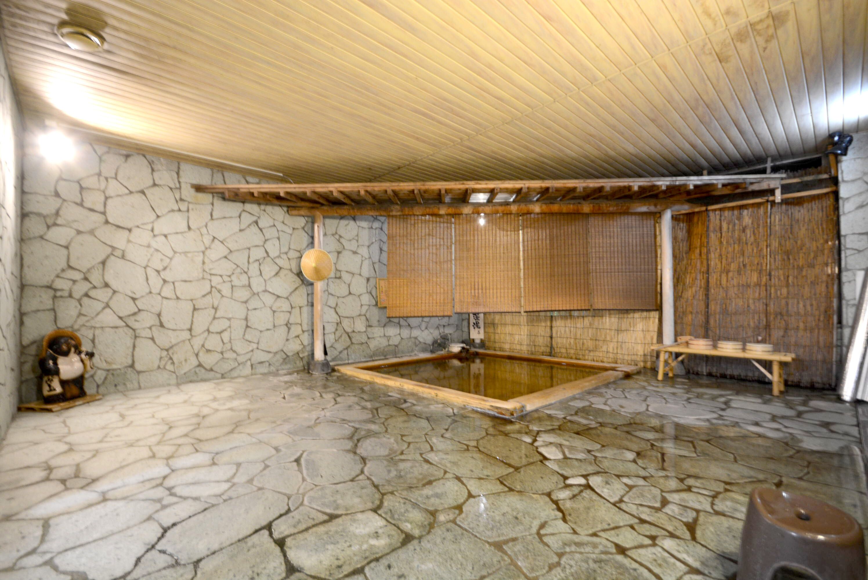 A traditional Japanese onsen with stone flooring, a wooden ceiling, and a bamboo screen wall.