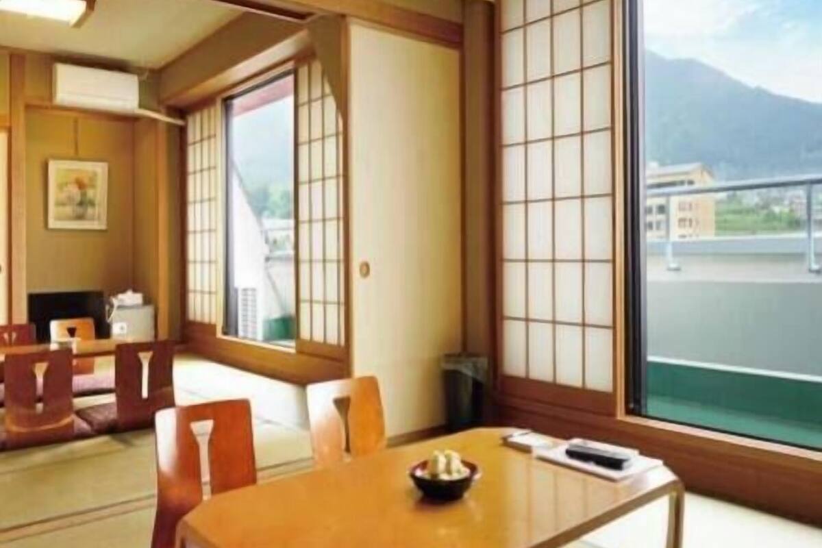 A traditional Japanese room with tatami flooring, a low table with a bowl, and large windows with a view of a mountain.