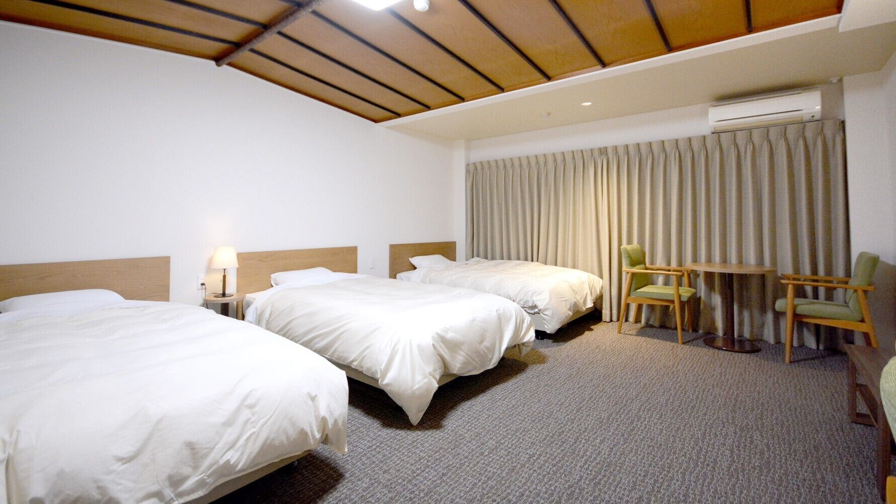 Une chambre d’hôtel avec deux lits, un bureau, une chaise, un appareil de climatisation et un rideau.
