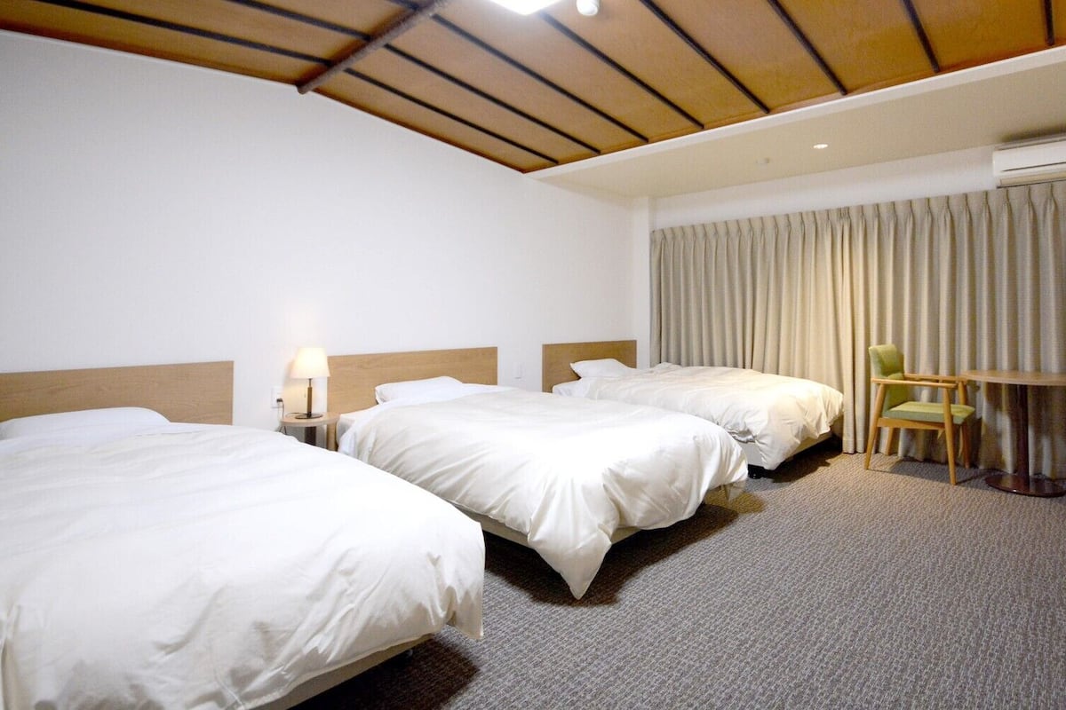 A hotel room with two beds, a desk, a chair, an air conditioning unit, and a curtain.