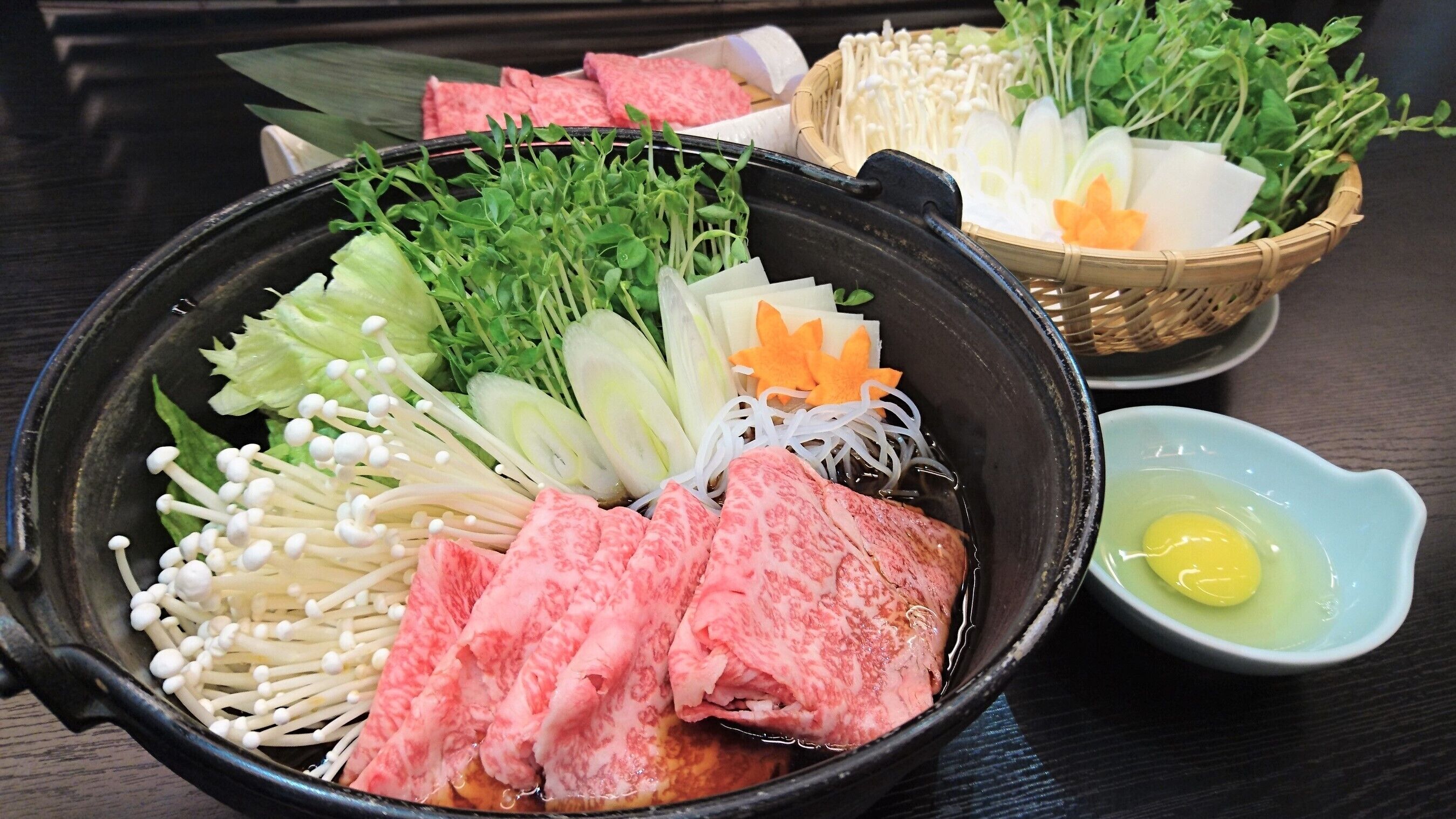 A bowl of assorted raw ingredients including mushrooms, leafy greens, and slices of meat, likely for a culinary preparation.