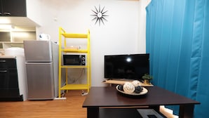 Una cocina moderna con refrigerador, microondas y estufa. Hay una estantería amarilla y un televisor de pantalla plana sobre una mesa de madera.