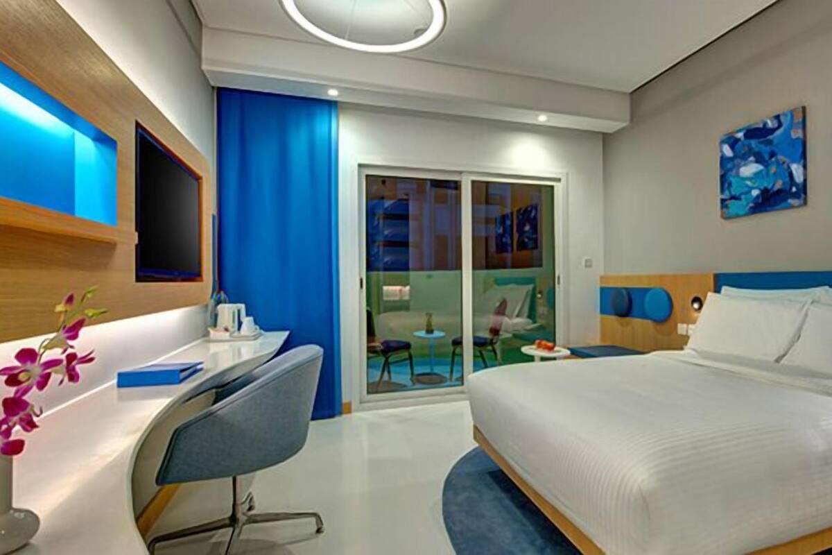 A modern hotel room with a bed, desk, chair, and a view of the outside.