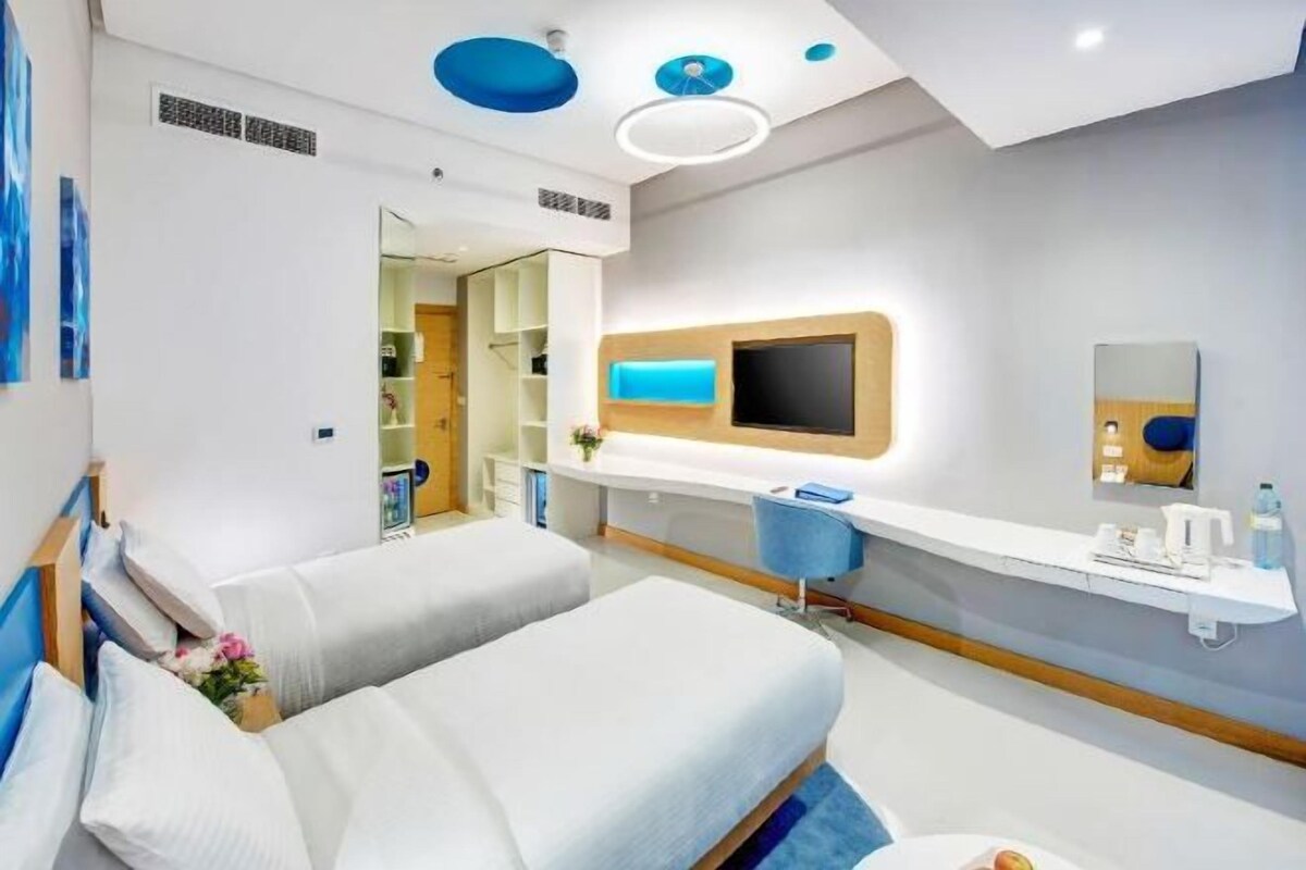 Quarto de hotel moderno com cama, escrivaninha, TV e banheiro.