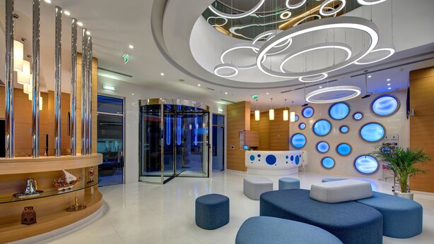 A modern lobby with a reception desk, seating areas, and a glass elevator. - Al Khoory Inn (Dubai)