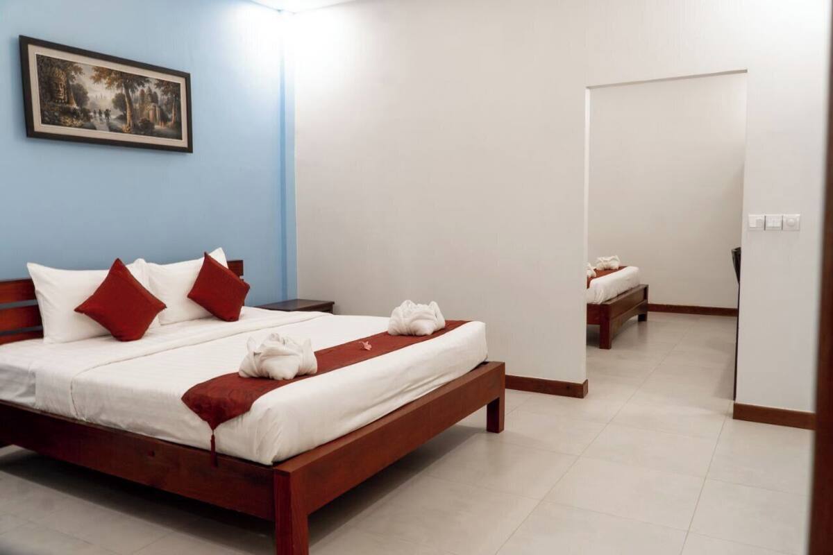 A neatly made bed with red pillows, a wooden headboard, and a painting on the wall.