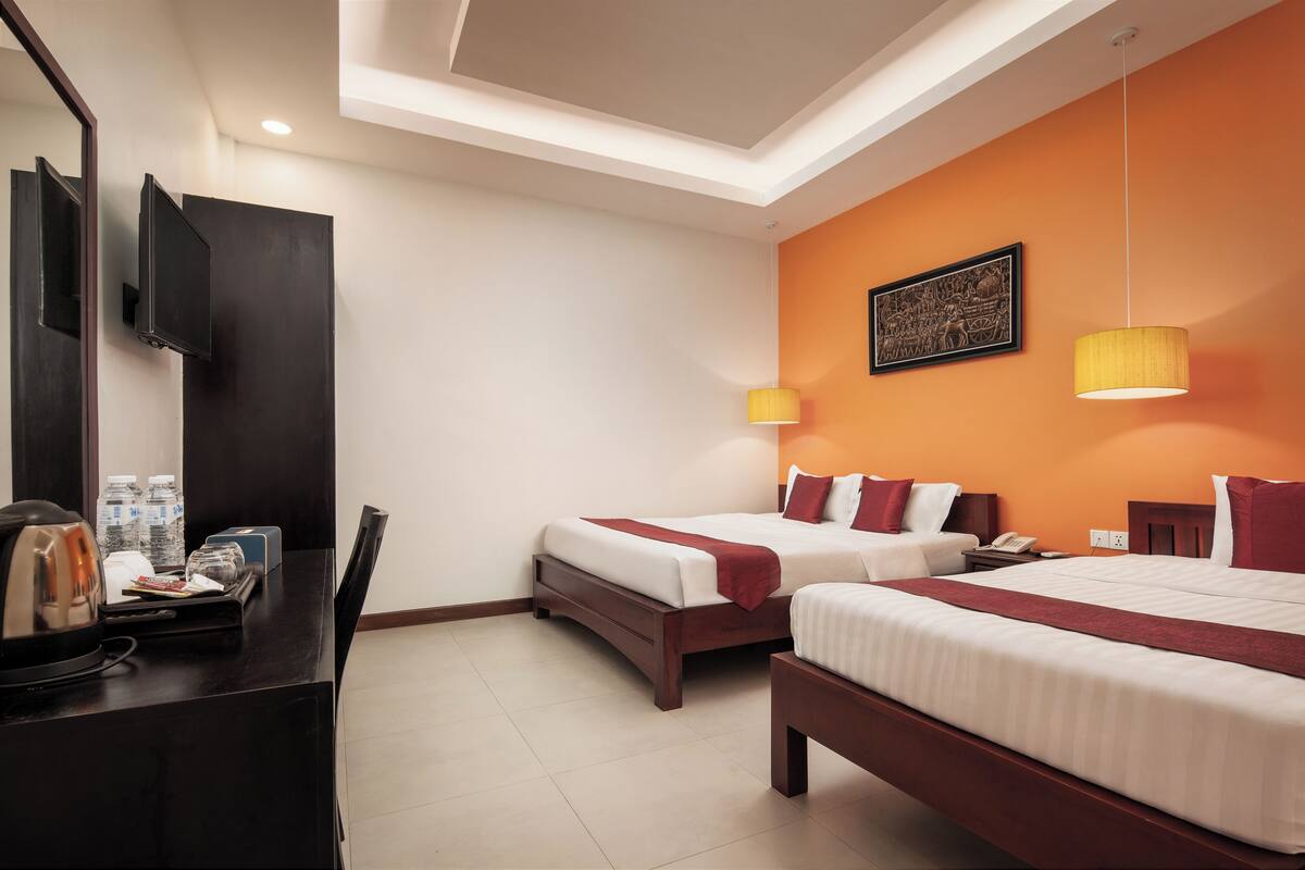 A hotel room with two beds, a desk with a telephone, and a mirror.