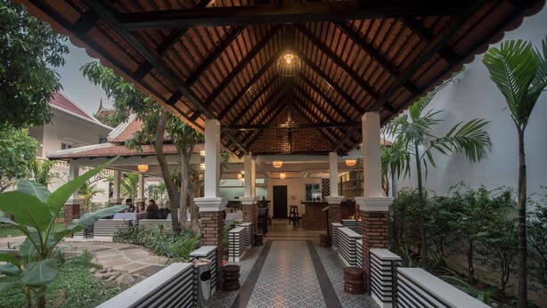 A covered outdoor area with a patterned floor, benches, and a central pathway leading to a building entrance. - Lavender Angkor Boutique (Siem Reap)