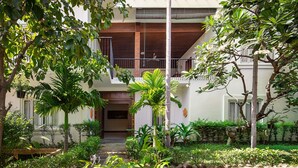 A courtyard with a wooden staircase leading to a balcony, surrounded by lush greenery and a white building with large windows. - Lavender Angkor Boutique (Siem Reap)