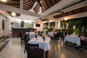 Un restaurante con mesas dispuestas para comer, una zona de bar y vistas a palmeras.