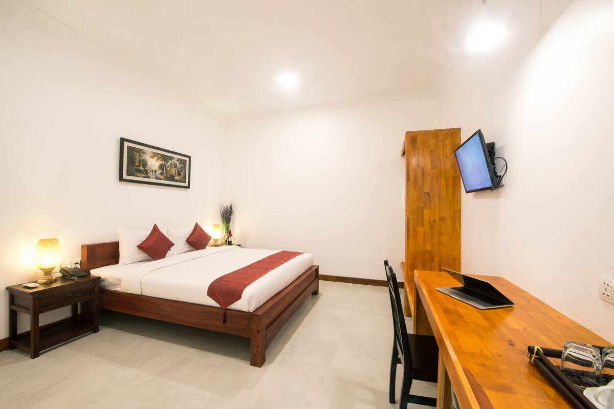 A bedroom with a bed, bedside table, lamp, and a desk with a laptop.