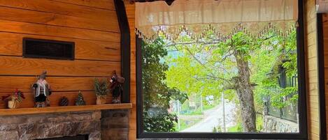 Ein gemütliches Blockhaushaus-Interieur mit Kamin aus Stein, Holzwänden, einem großen Fenster mit Blick und einer Sitzbank.
