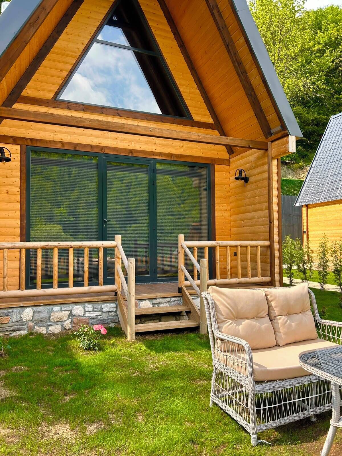 A log cabin with a porch, stone steps, and wicker furniture.