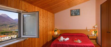 Een kamer met houten lambrisering, een bed, een raam met uitzicht op bergen en een schilderij aan de muur.