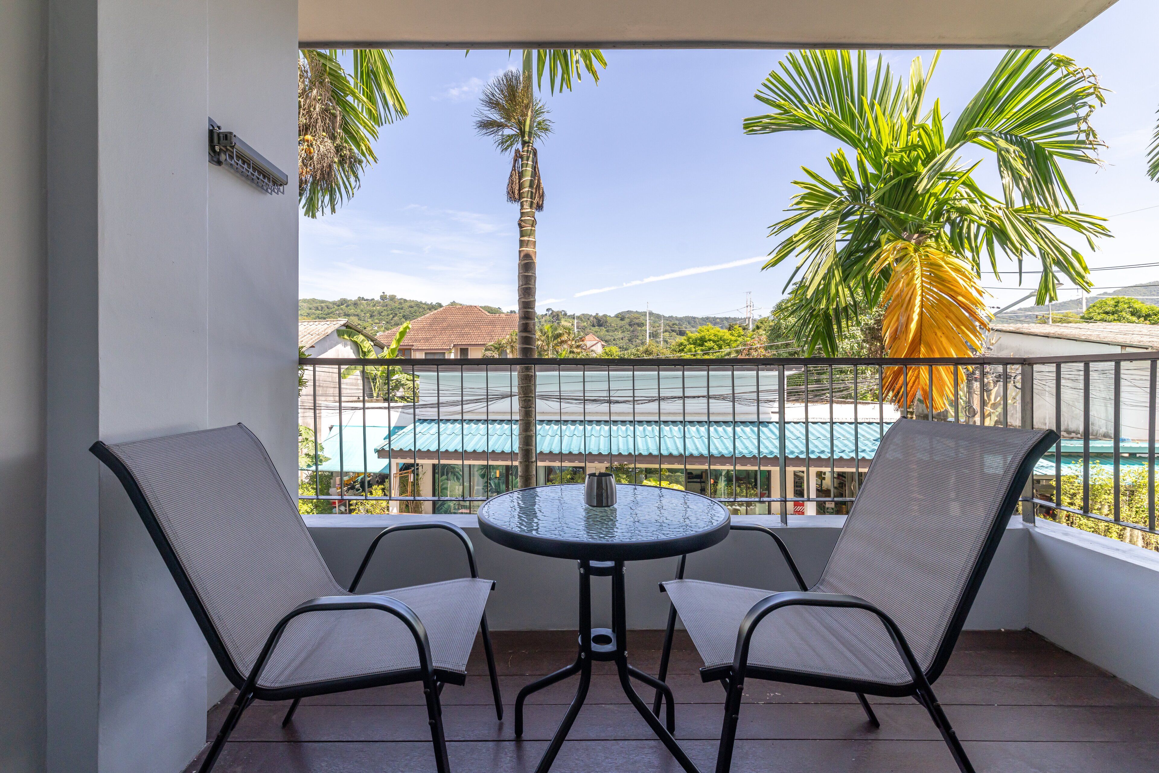 A balcony with two chairs and a table, overlooking a swimming pool and palm trees.