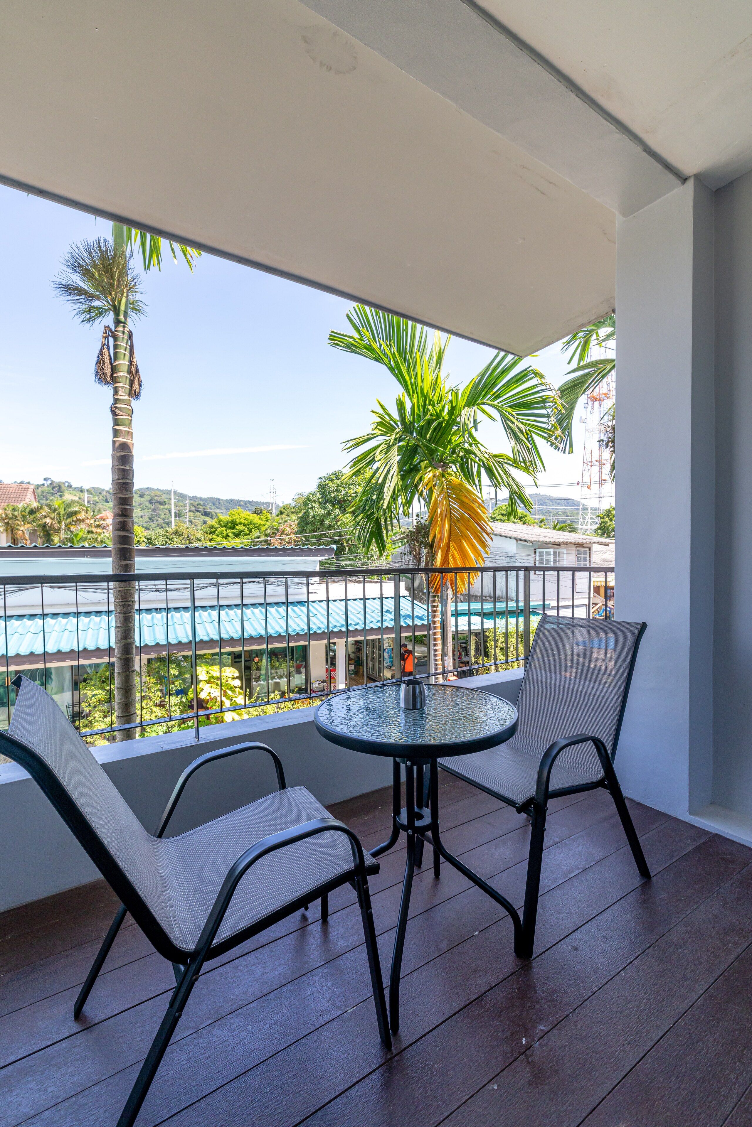 A balcony with two chairs and a table, overlooking a pool and greenery.