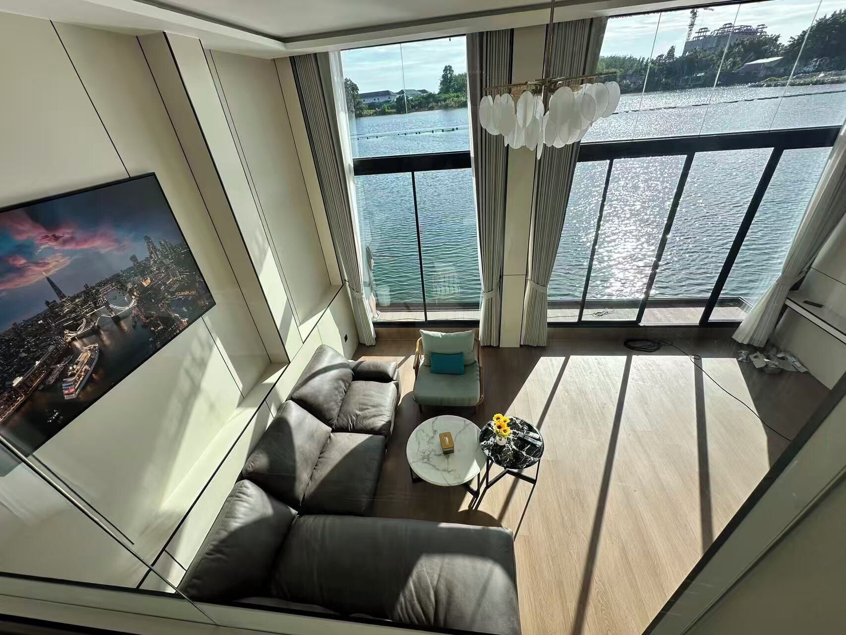 Un salon moderne doté d’une grande fenêtre donnant sur un plan d’eau, d’un canapé, d’une table basse et d’un tableau représentant un paysage urbain.