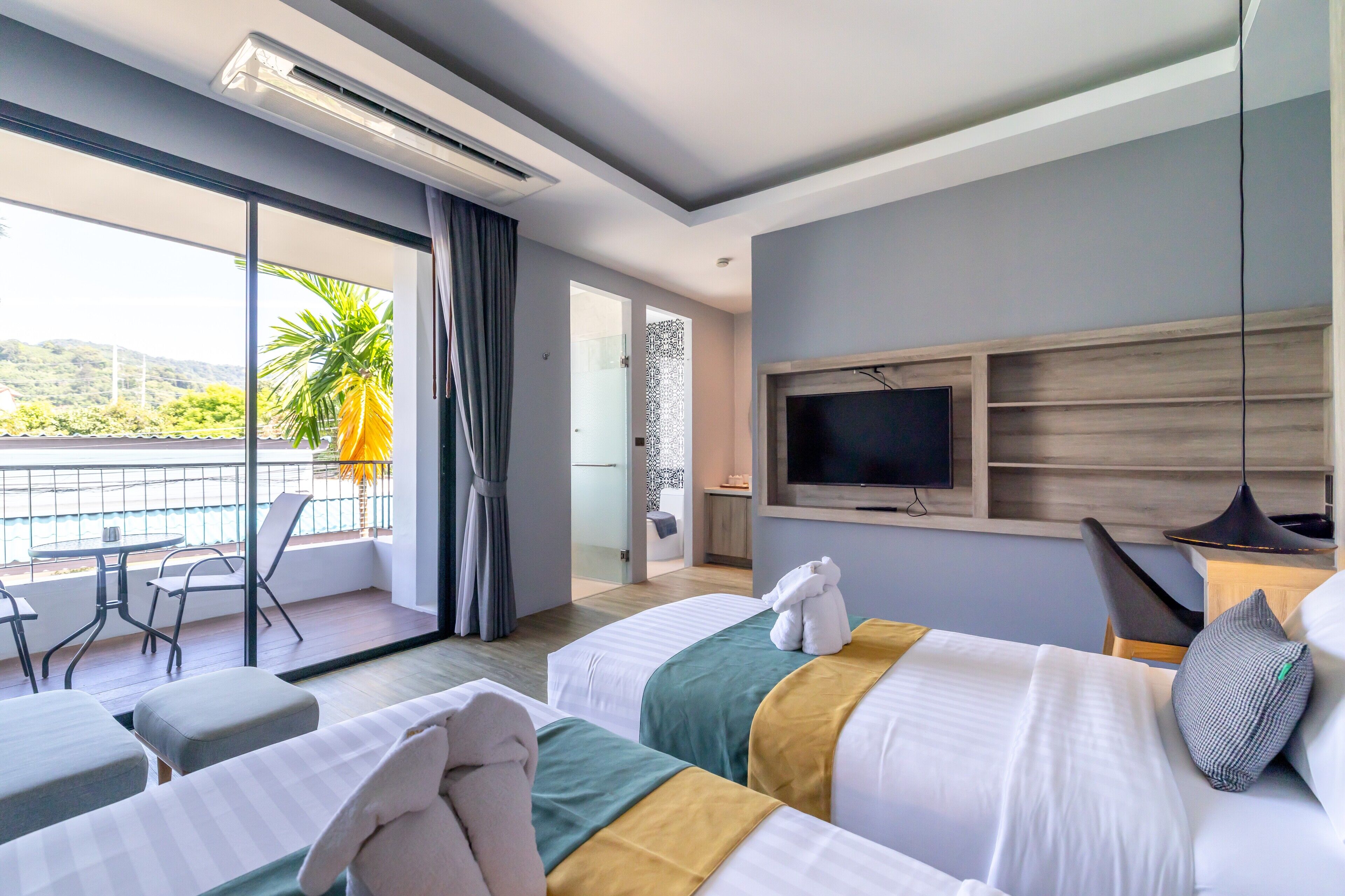 Une chambre d’hôtel avec deux lits, une télévision, un balcon avec une table et des chaises, et une vue sur l’extérieur.