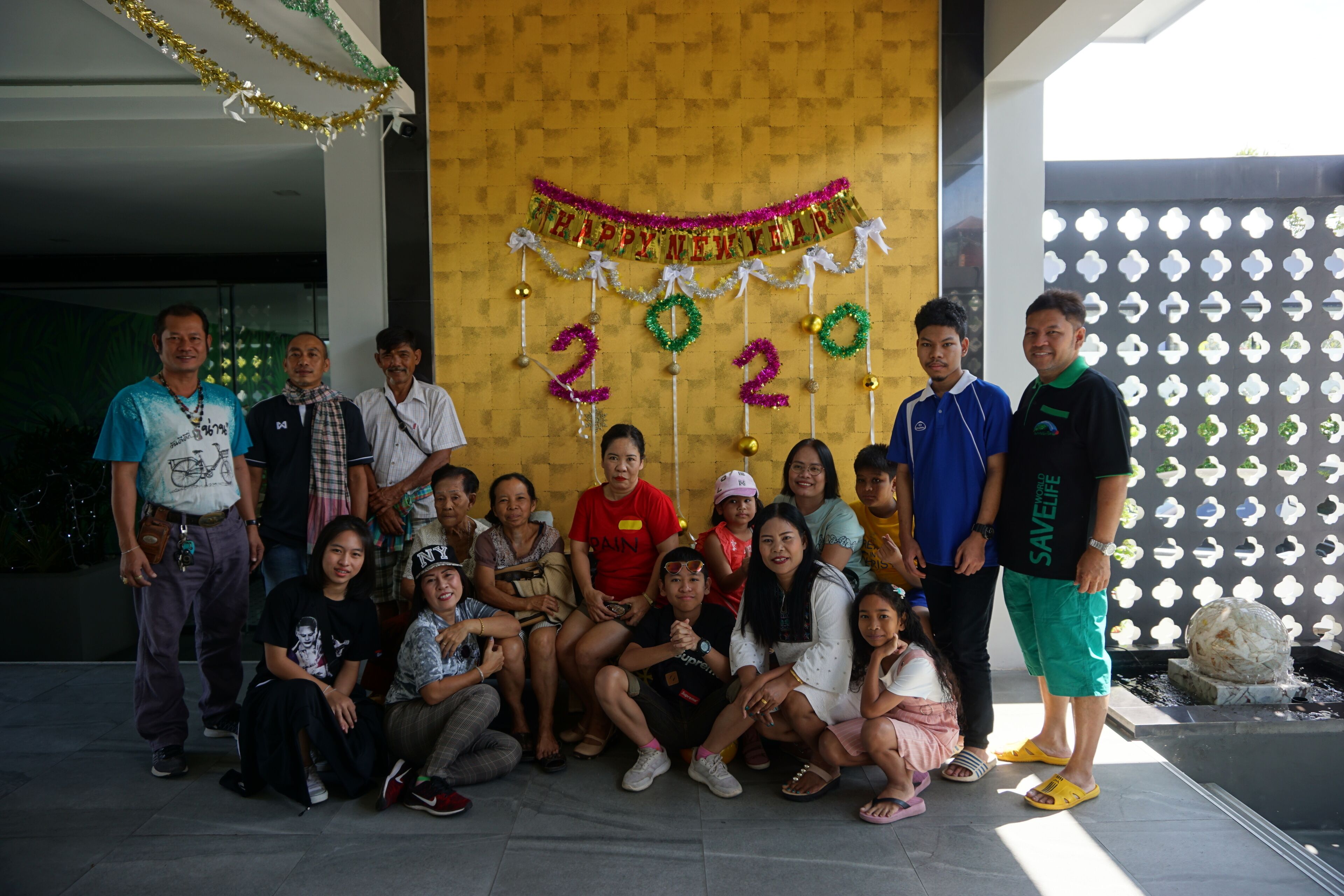 A group of people posing in front of a wall with a 'Happy New Year 2020' banner and decorative numbers.