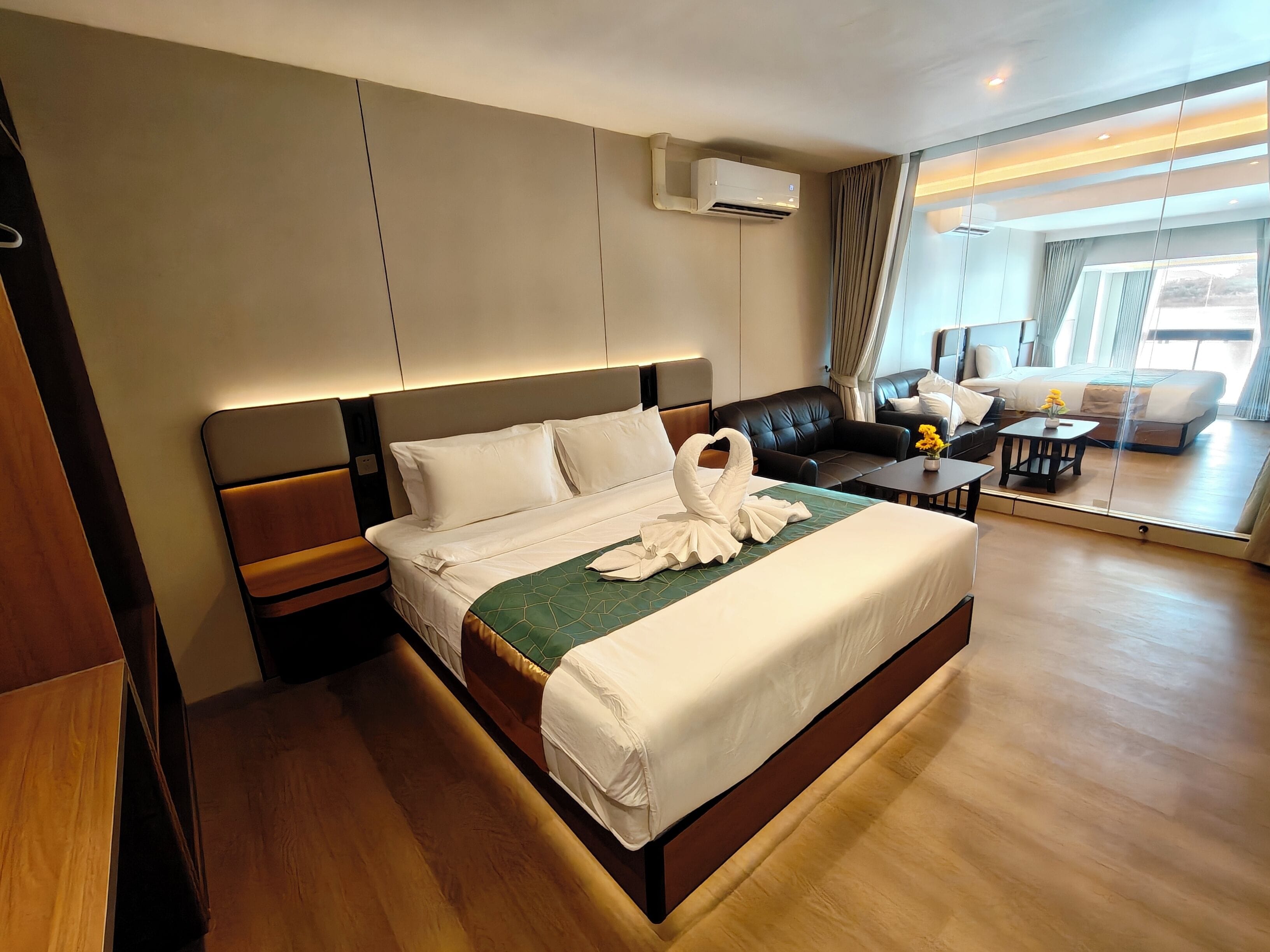 A hotel room with a large bed, a sofa, a small table, and a view of the outdoors through a glass wall.