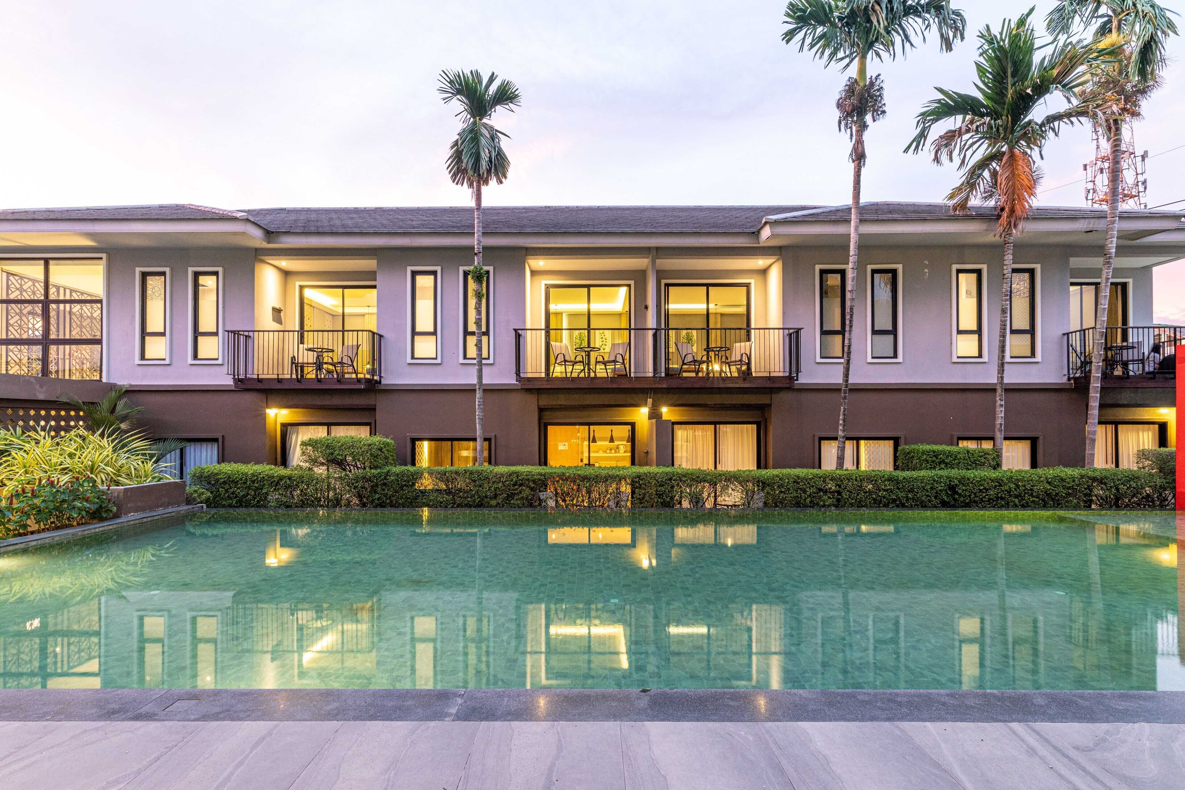 A hotel with a swimming pool, multiple balconies, and palm trees.