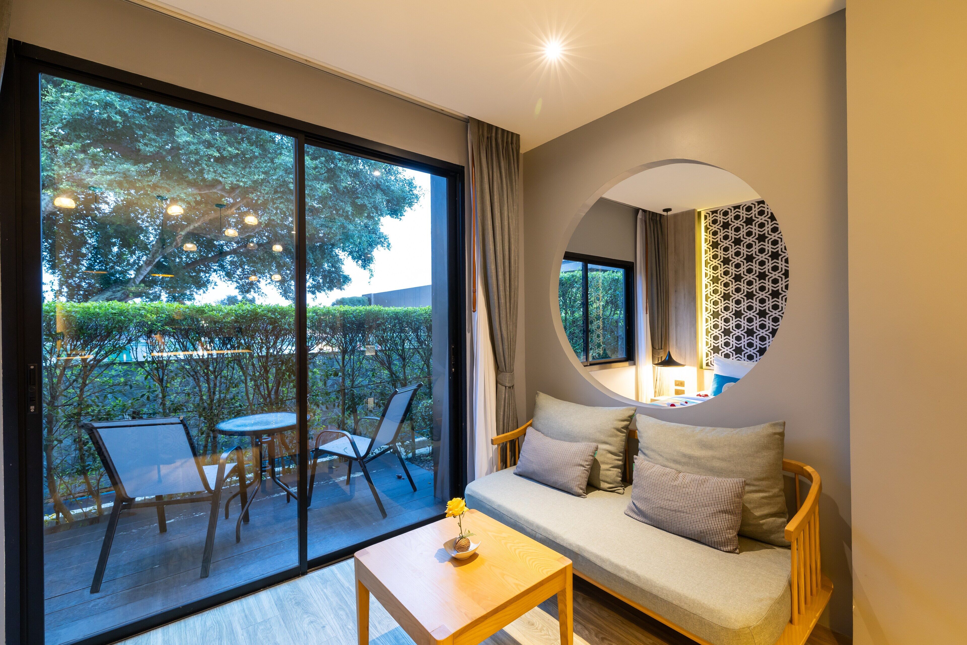 A modern living room with a sofa, a small table with a vase, and a large window overlooking a garden.