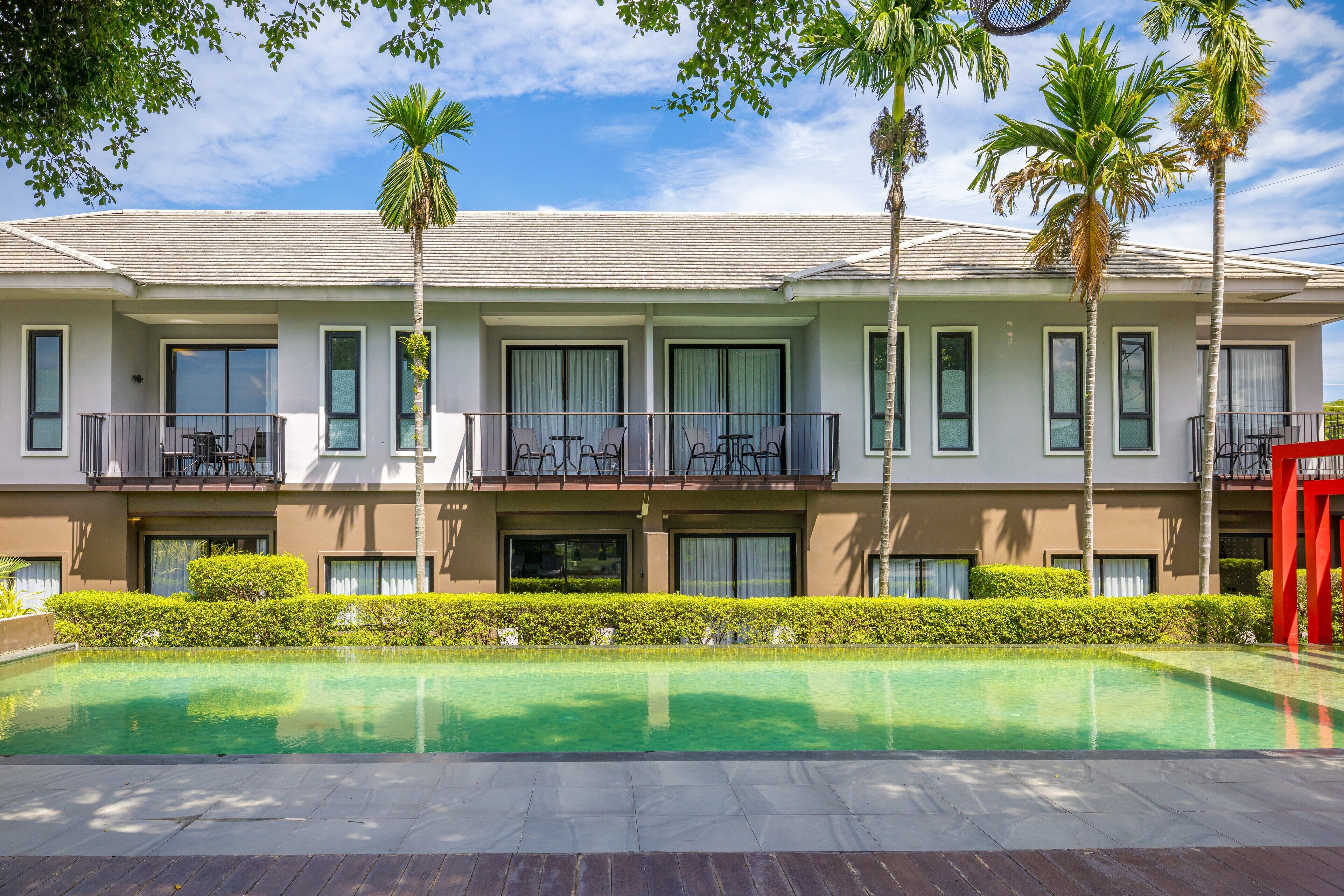 A modern hotel with a swimming pool, balconies with outdoor furniture, and palm trees.