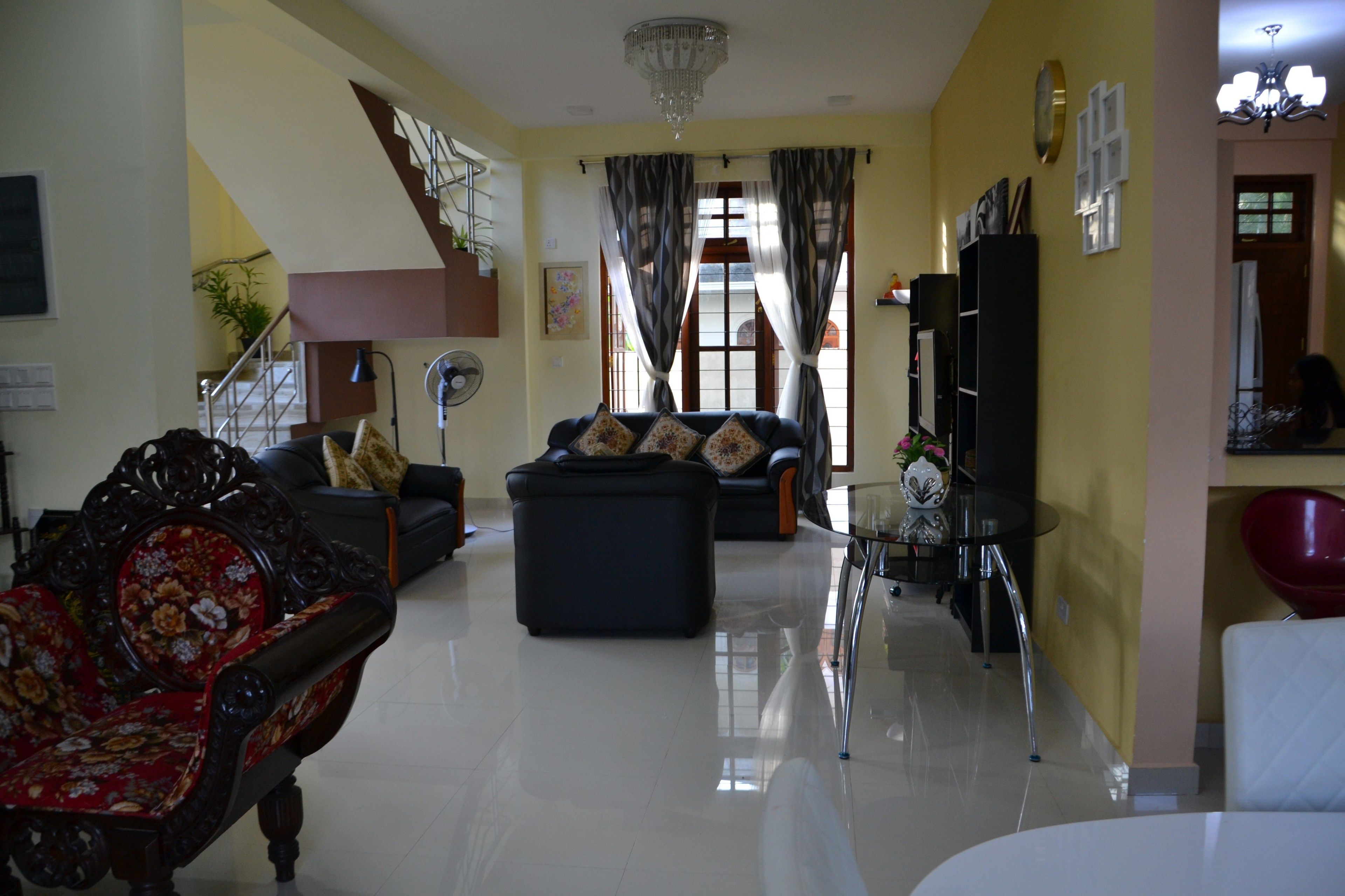 Amplio salón con escalera, un sofá negro, un sillón floral rojo y una mesa de centro de vidrio.