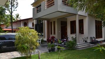 A two-story house with a balcony, a car parked in front, and several potted plants.