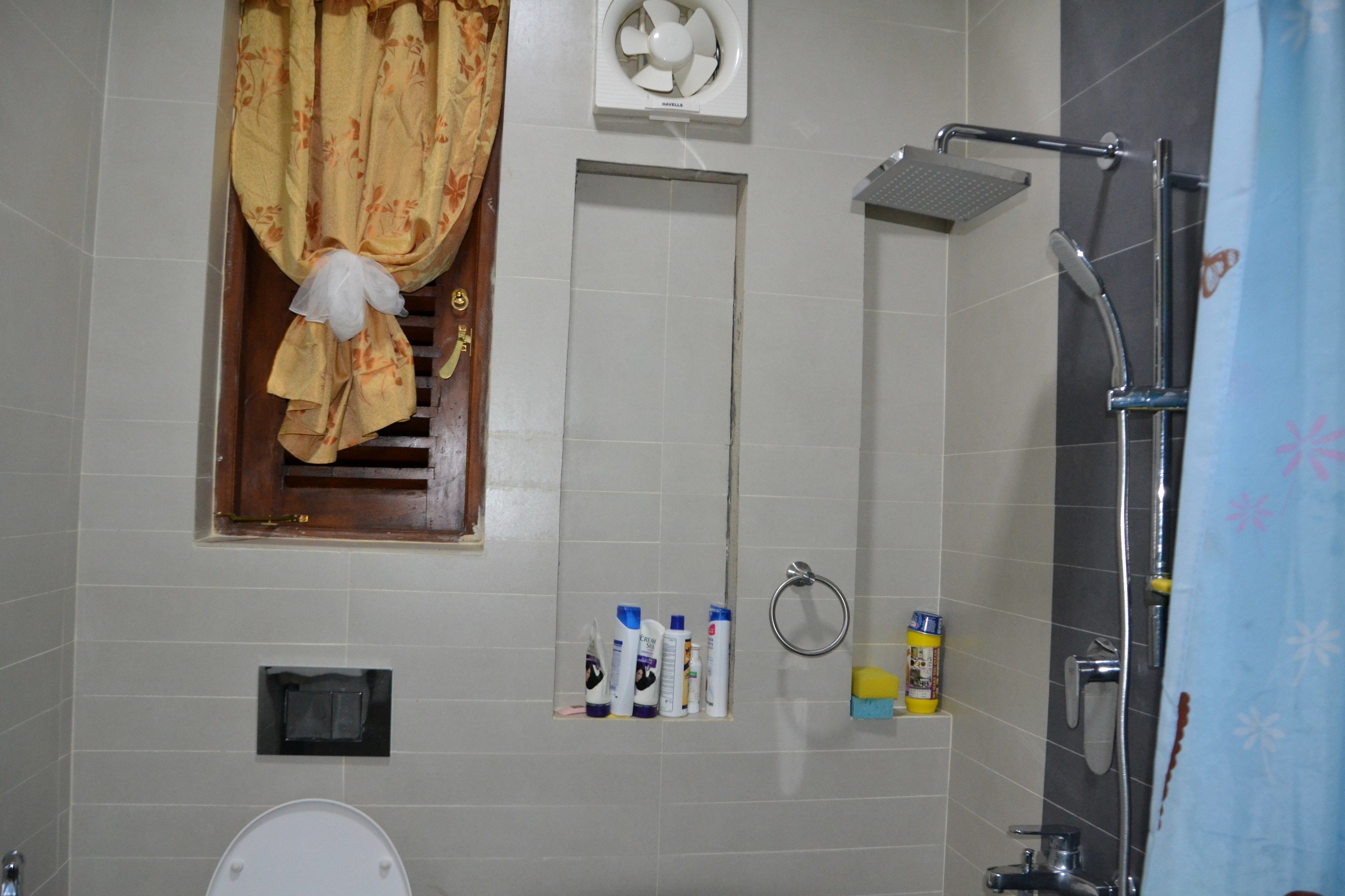 A bathroom with a toilet, a shower, a fan, and toiletries on the wall.