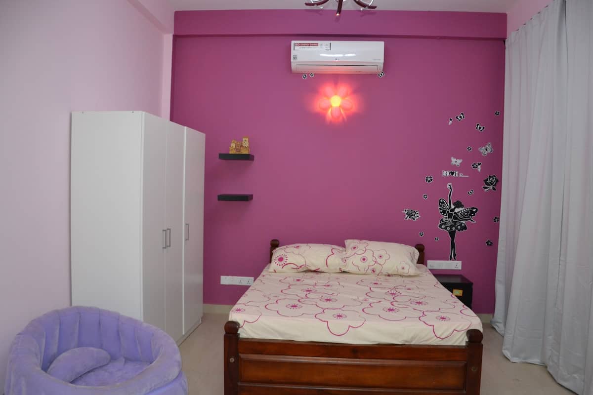 A bedroom with a bed, a wardrobe, a chair, and a wall-mounted air conditioner.
