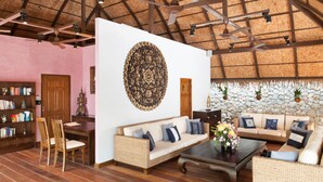 A spacious room with a high ceiling, a large decorative wall piece, a sofa set, a dining table, and a bookshelf. - Shanaya Residence Ocean View Kata (Karon)