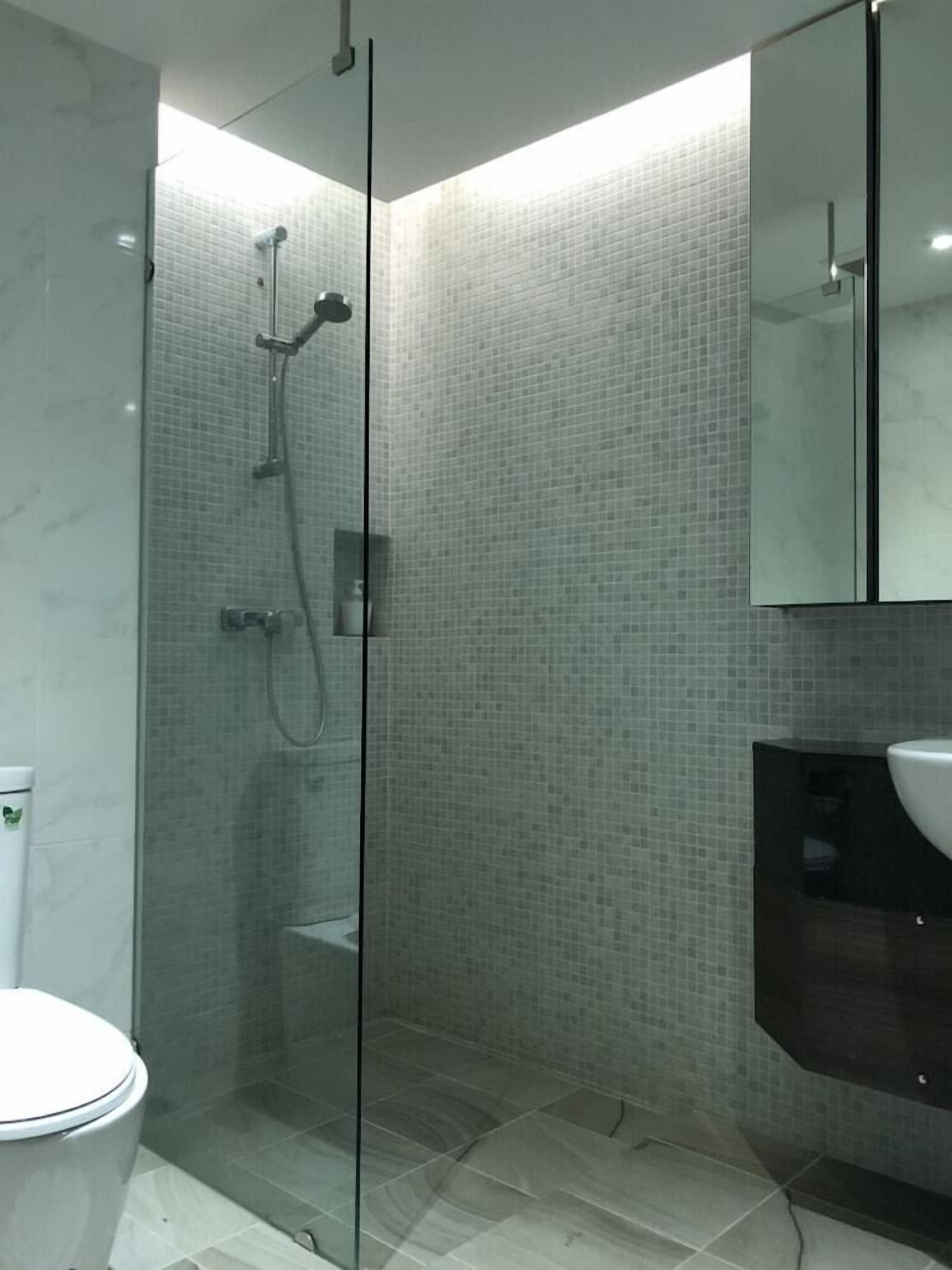 Une salle de bain moderne avec une douche à parois de verre, des toilettes blanches et un lavabo aux tons foncés.