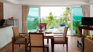 A dining area with a table set for four, a television, and a kitchen area with a coffee maker. - Shanaya Residence Ocean View Kata (Karon)