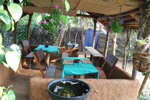 Un área de comedor al aire libre con mesas y sillas, una maceta colgante y un tazón grande con flores.