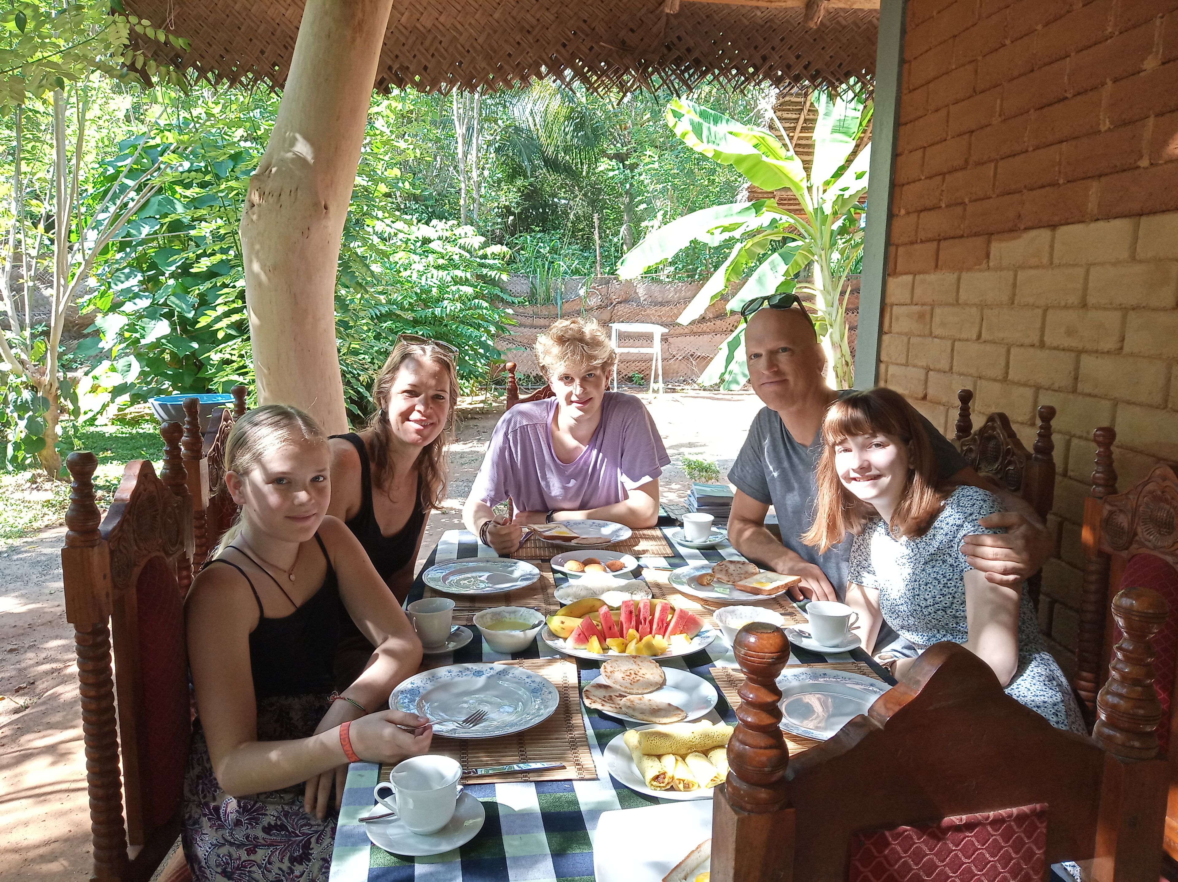 A group of people dining at an outdoor table with various dishes and drinks.