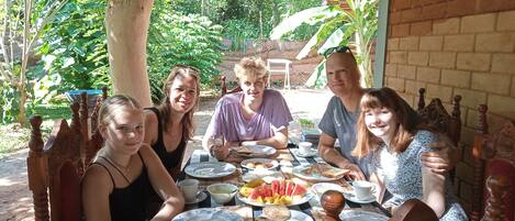 A group of people dining at an outdoor table with various dishes and drinks.