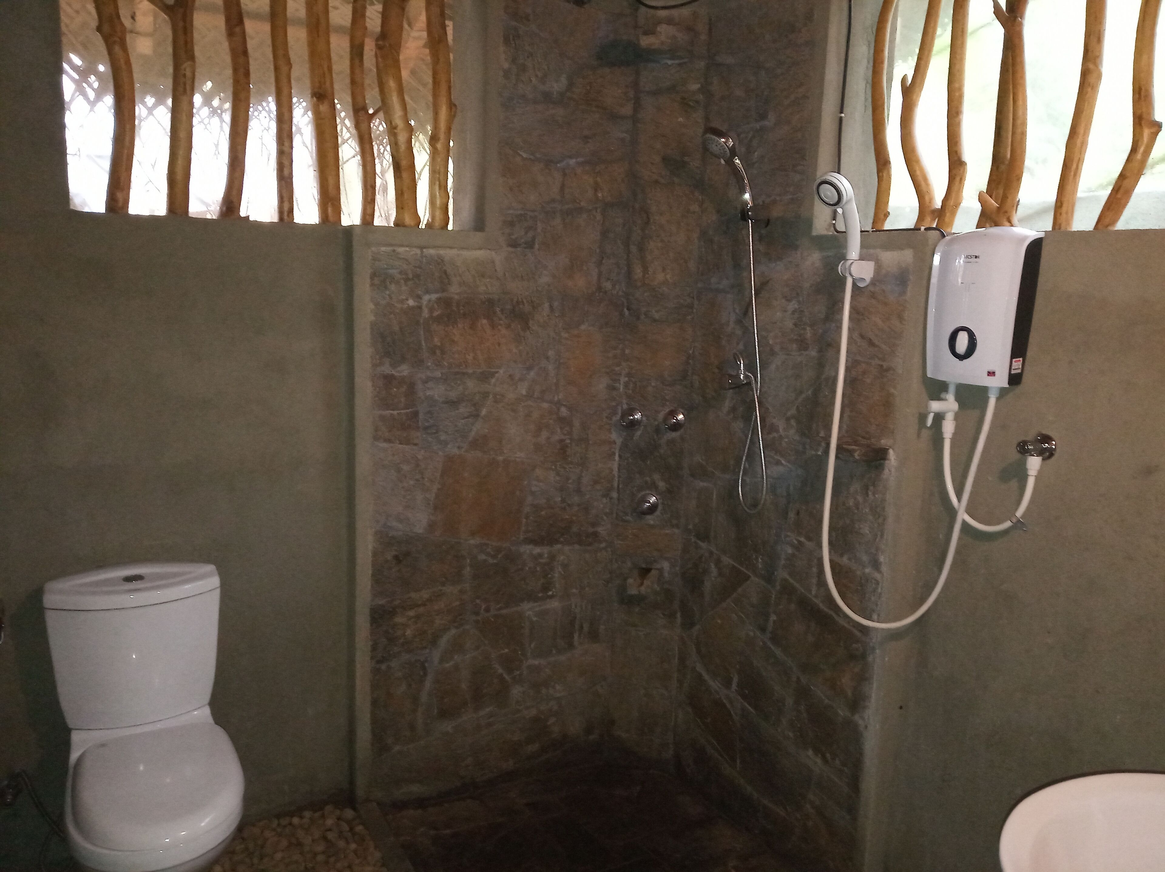A bathroom with a stone shower enclosure, a toilet, and a water heater.